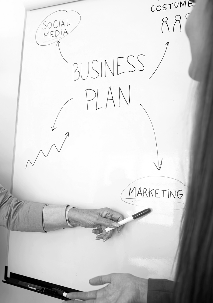 Senior caucasian business woman showing young female coworker business plan on white board in the office. Business concept.